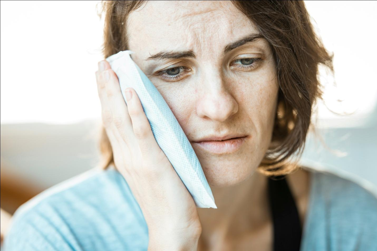 a woman holding an ice pack to her cheek