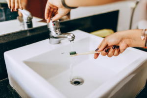 A person holding her toothbrush under the water in a sink