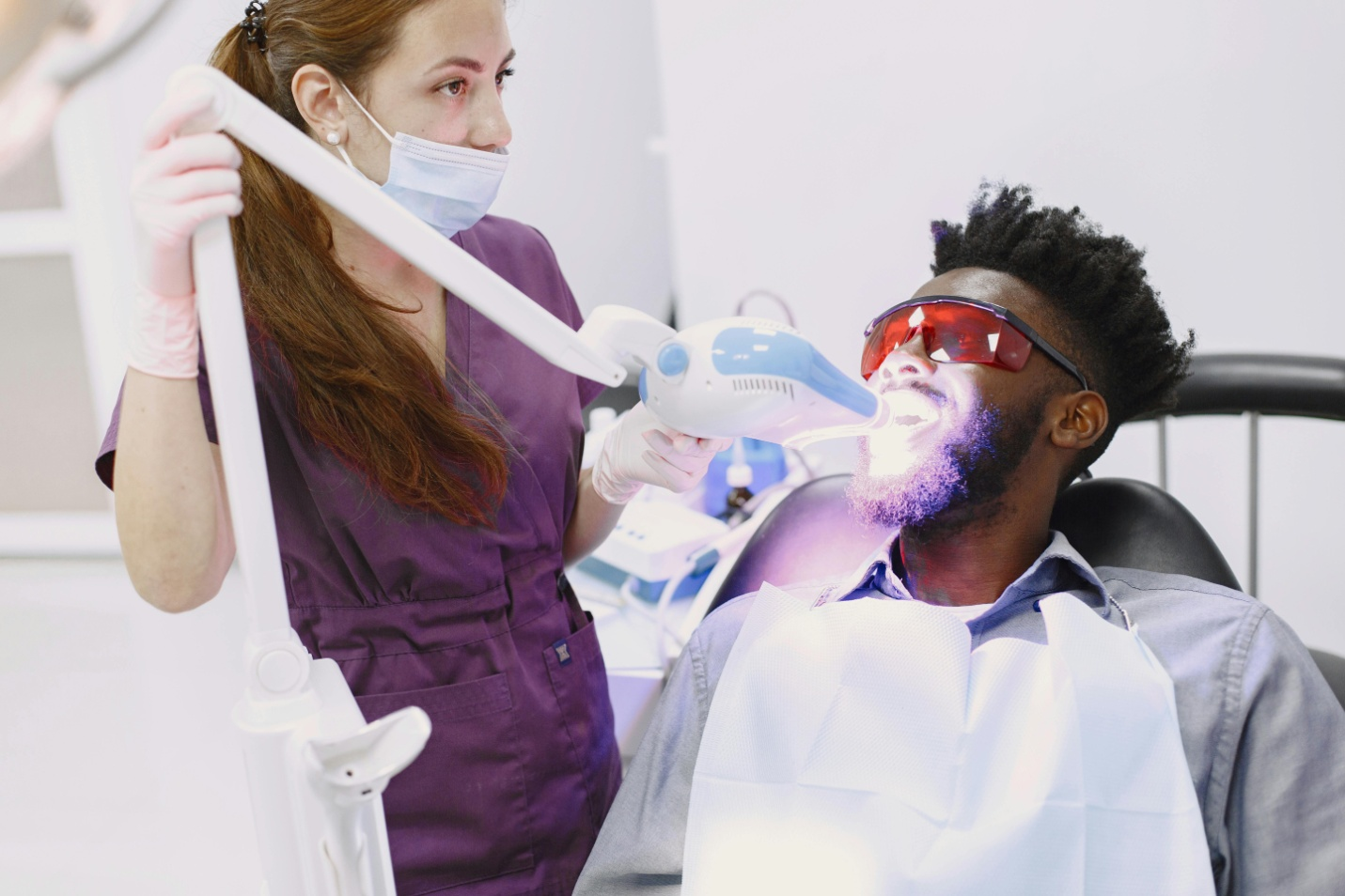 dentist performing teeth whitening service on a patient sitting in the dental chair