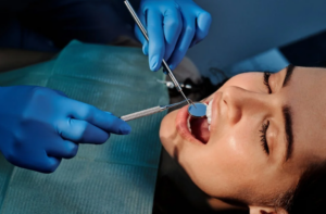 a person wearing blue latex gloves inspecting a patient's mouth with dental equipment