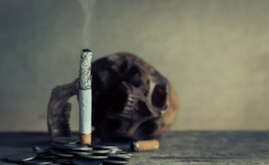 focused shot of a lit cigarette with a skull in the background